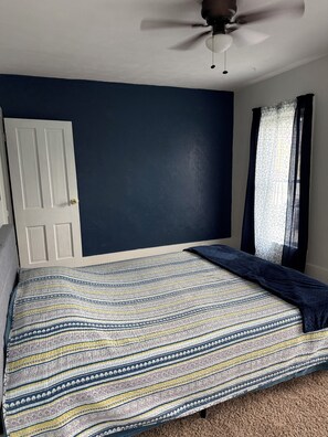 A bedroom with a bed, a ceiling fan, a door, and a window with curtains.