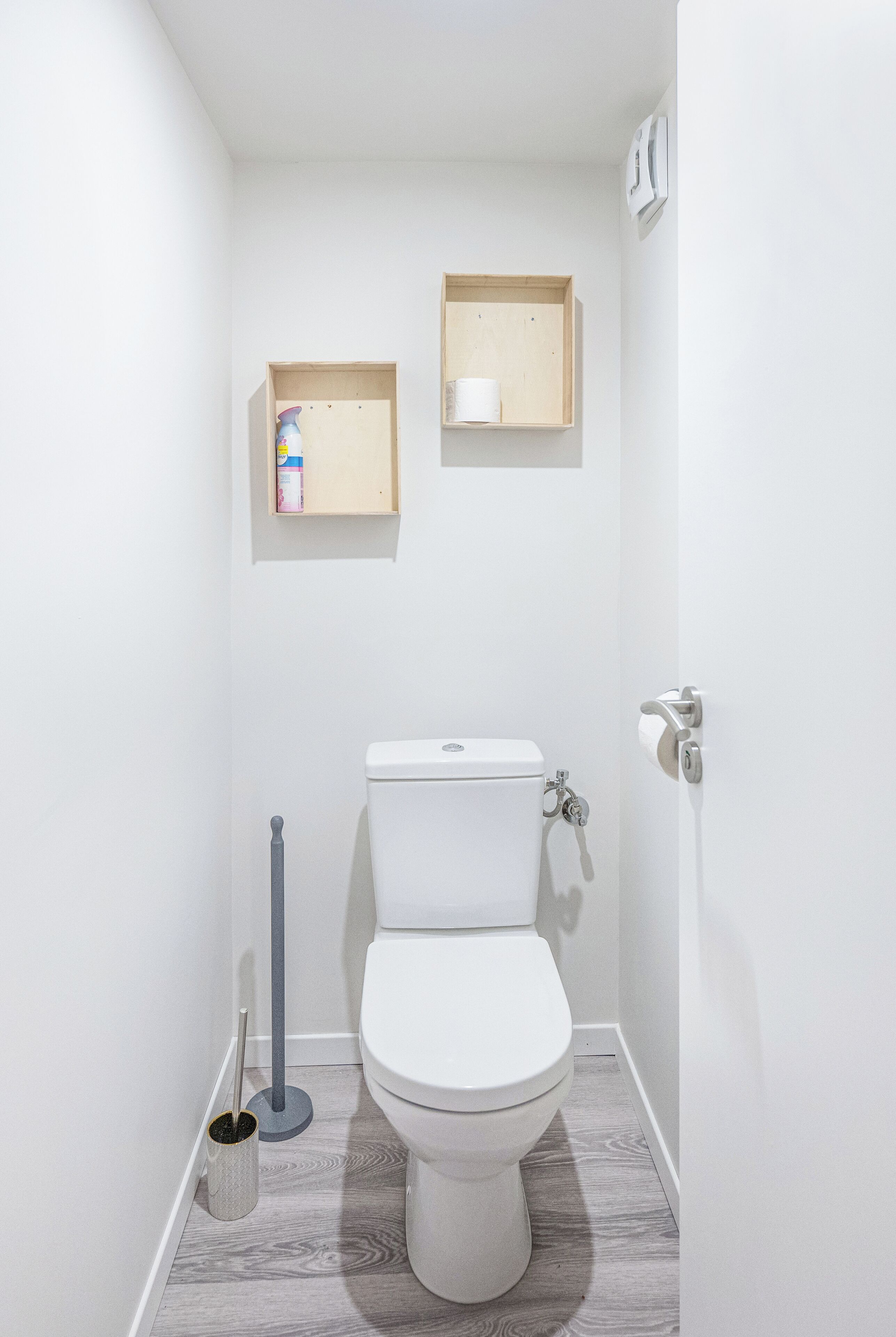 Een kleine, witte badkamer met een toilet, een bidet en twee houten planken boven het toilet.