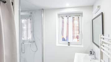 A modern bathroom with a glass shower enclosure, a white sink, and a window with curtains.