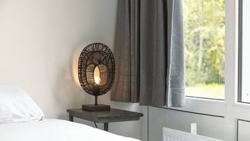 Una cama con ropa de cama blanca, una mesita de noche con una lámpara negra y una ventana con cortinas.