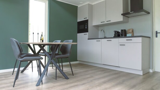 A modern kitchen with white cabinets, a microwave, and a sink. There is a dining table with chairs. - The bungalow Palthe Comfort offers comfort and tranquility in nature for 4 people, with modern amenities and a lovely terrace. (Nieuw Heeten)