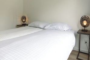 En säng med vita sängkläder, två sängbord med lampor och ett vägguttag.