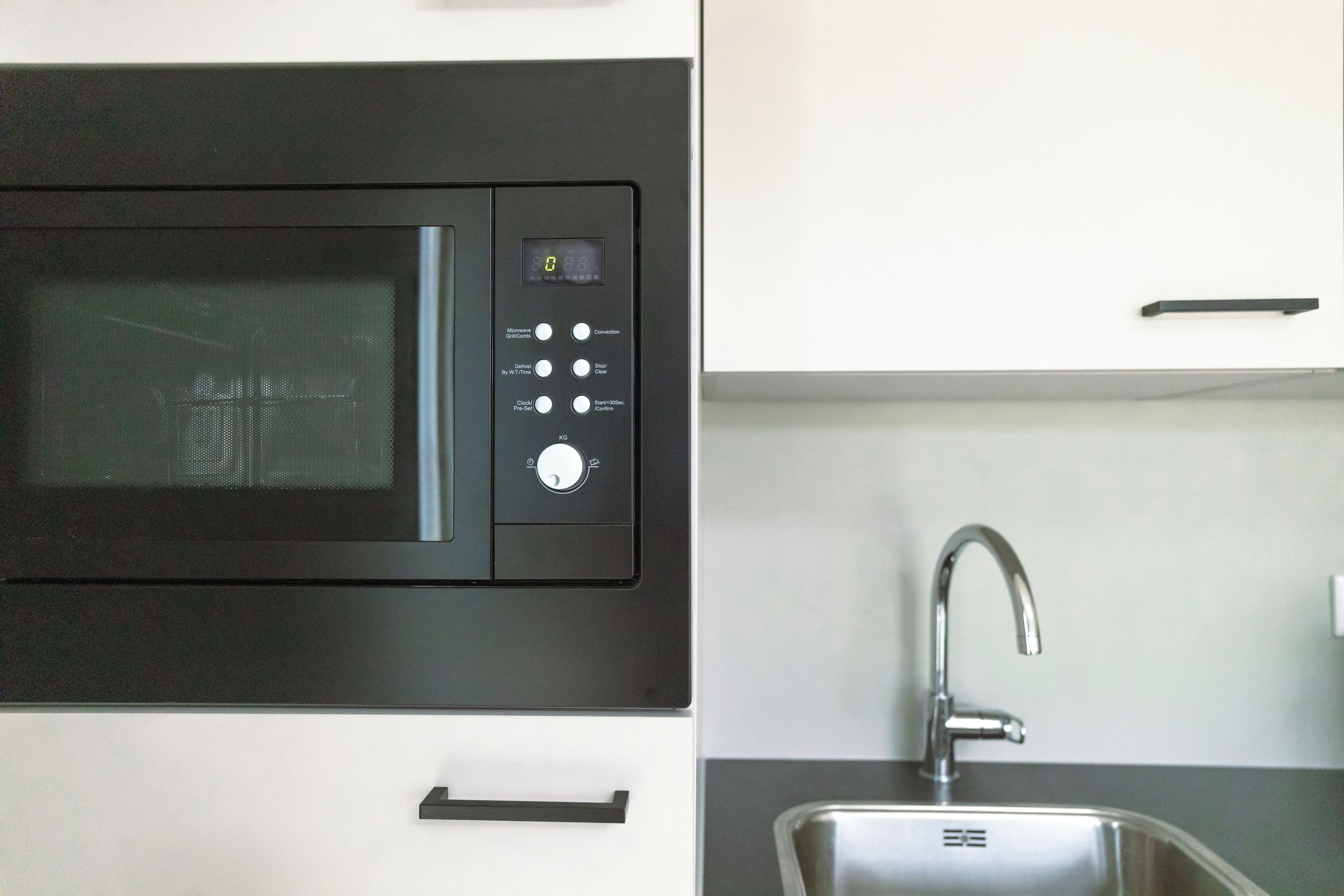 Een keuken met een magnetron, een spoelbak en een kast.