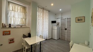 A small kitchen with a dining table, chairs, a refrigerator, and a window with curtains. - Quiet Central Apartment (Roma)