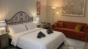 A hotel room with a bed, a nightstand, a lamp, a sofa, and a painting on the wall. - Quiet Central Apartment (Roma)