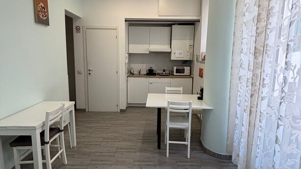 A compact kitchen with white cabinets, a microwave, and a dining area with a table and chairs. - Quiet Central Apartment (Roma)