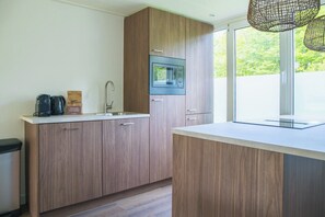 A modern kitchen with wooden cabinets, a built-in microwave, and a window providing a view of greenery. - The Palthe Premium Living bungalow has been recently fully renovated and features a stylish, modern interior. It offers all the comfort for 4 people, surrounded by nature, with a lovely terrace to relax outdoors. (Nieuw Heeten)