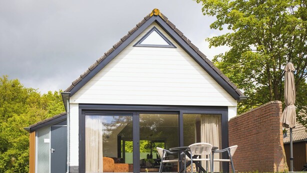 A house with a gabled roof, large sliding glass doors, and a patio with outdoor furniture. - The Palthe Premium Living bungalow has been recently fully renovated and features a stylish, modern interior. It offers all the comfort for 4 people, surrounded by nature, with a lovely terrace to relax outdoors. (Nieuw Heeten)