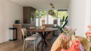 A modern kitchen with wooden cabinets, a dining table with chairs, and a view of greenery outside. - The Palthe Premium Living bungalow has been recently fully renovated and features a stylish, modern interior. It offers all the comfort for 4 people, surrounded by nature, with a lovely terrace to relax outdoors. (Nieuw Heeten)