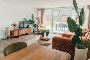 Een moderne woonkamer met een houten salontafel, een televisie op een houten dressoir, een gestreept fauteuil en een groot raam met uitzicht.