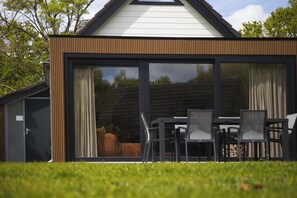 Une maison moderne dotée d’une grande porte-fenêtre coulissante, d’un coin repas avec des chaises et d’un jardin visible.