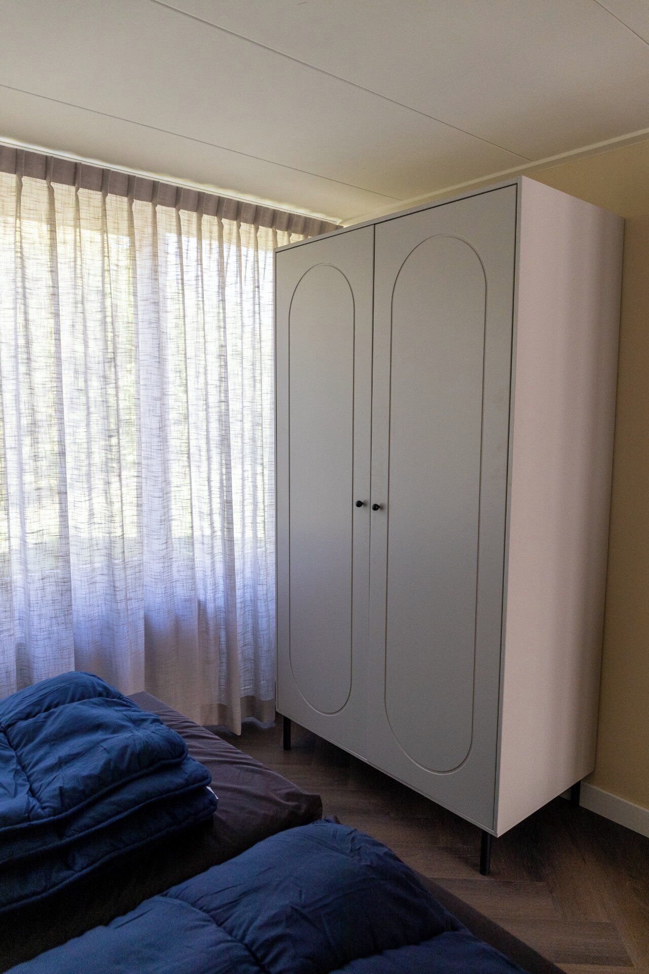 A bedroom with a wardrobe, a bed, and a window with curtains.