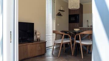 Een moderne eethoek met een houten tafel en stoelen, een televisie en een keuken op de achtergrond.