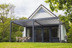 A house with a covered patio, a glass door entrance, and a lawn with chairs.
