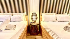Habitación de hotel con dos camas, una mesita redonda con una lámpara y paneles de madera en las paredes.