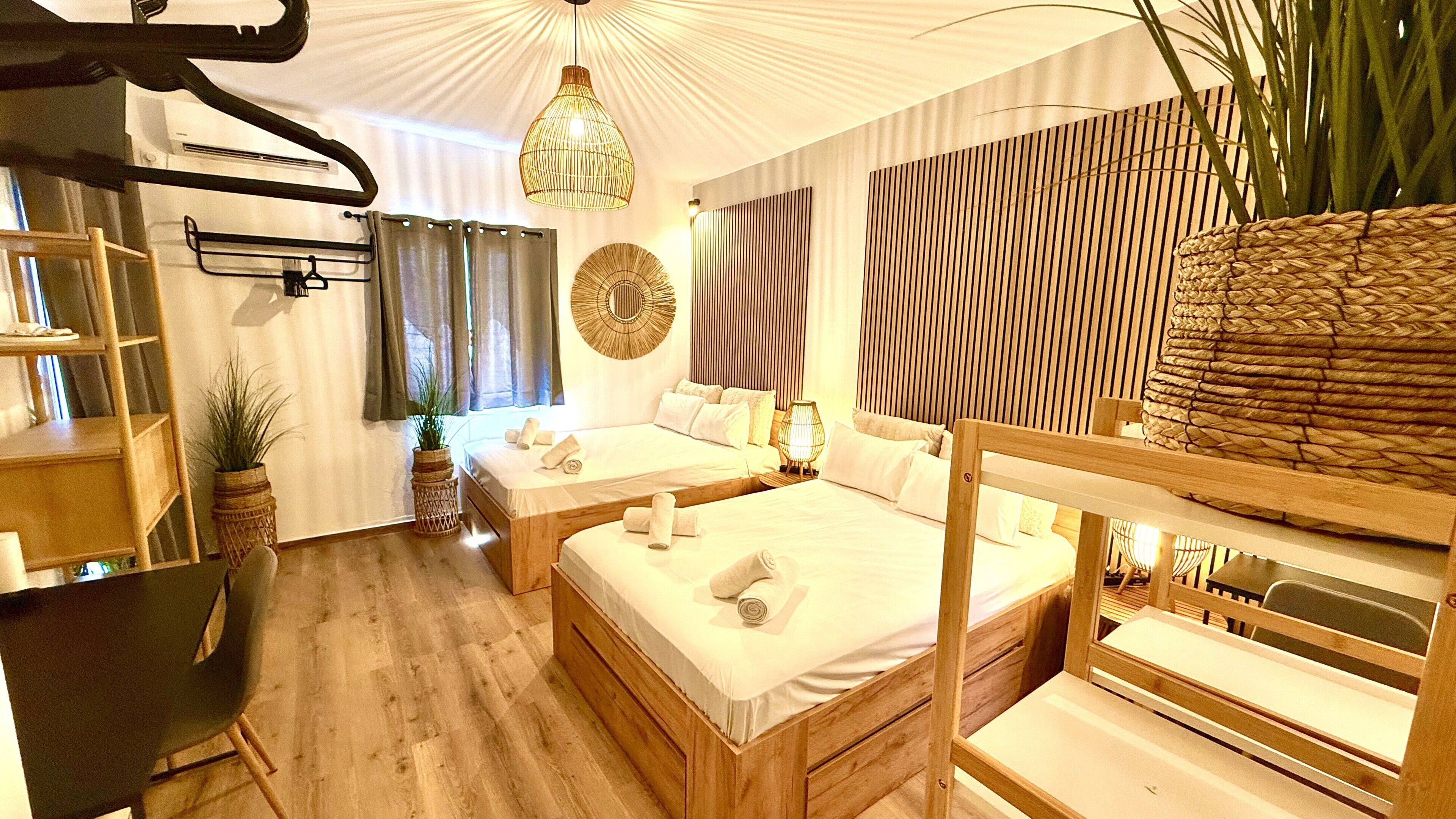 Ein Hotelzimmer mit zwei Betten, Holzboden, einem großen gewebten Korb und einem an der Wand befestigten Regal.