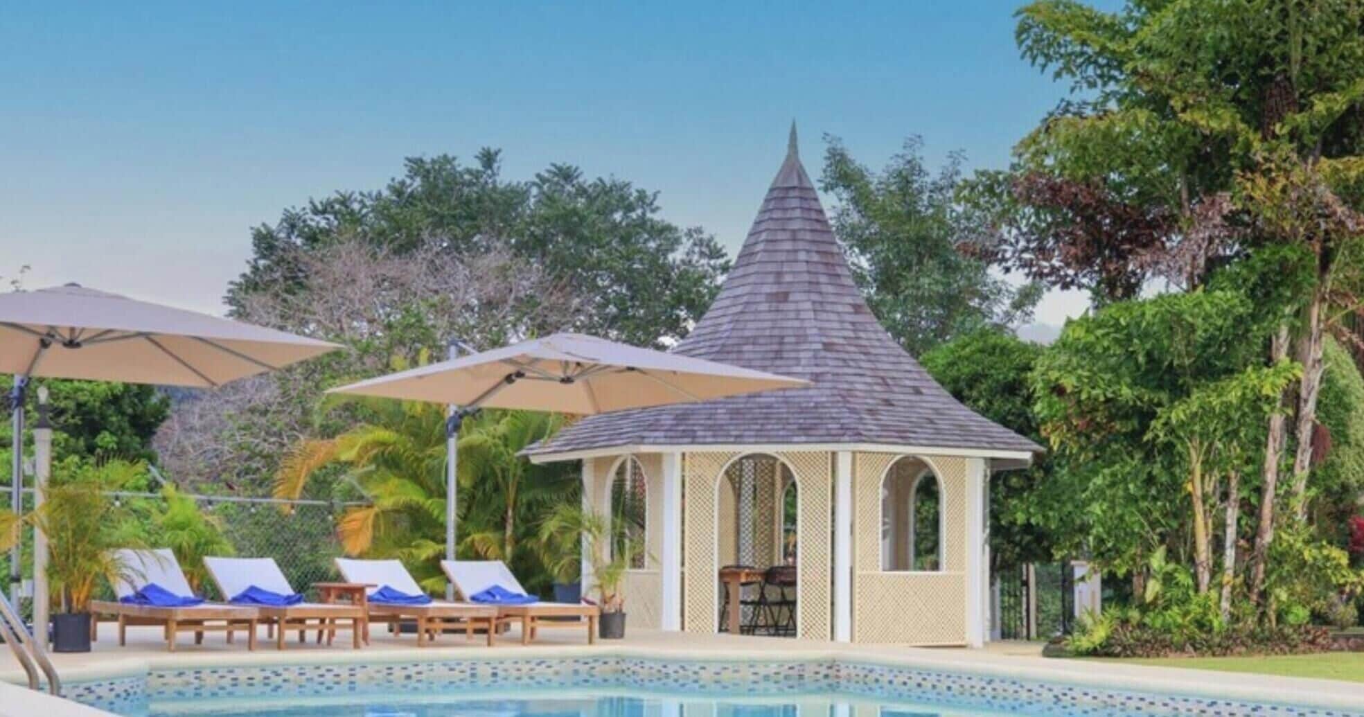 A pool area with lounge chairs and umbrellas, a gazebo, and lush greenery.