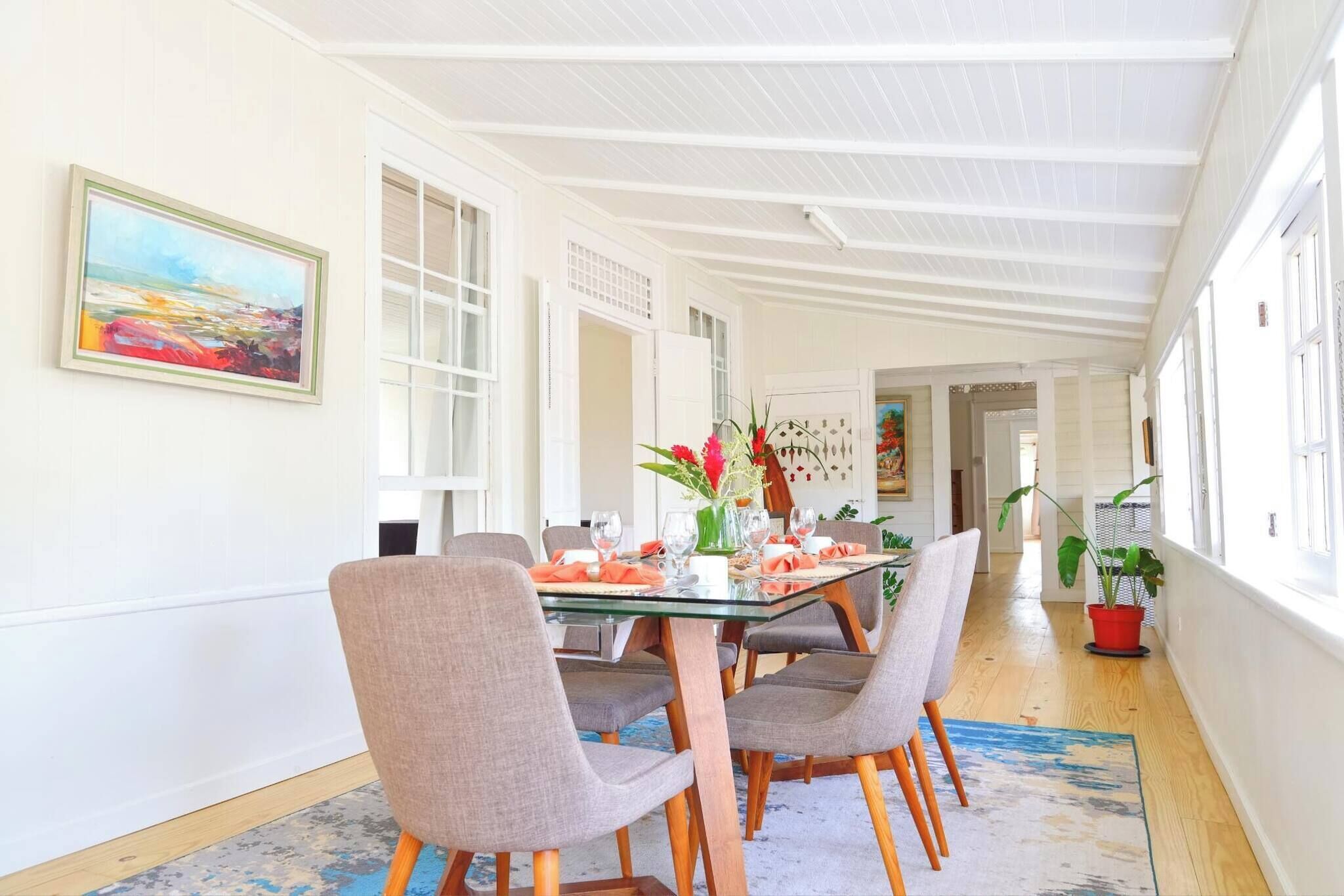 A dining area with a glass table, grey upholstered chairs, and a vase with flowers.
