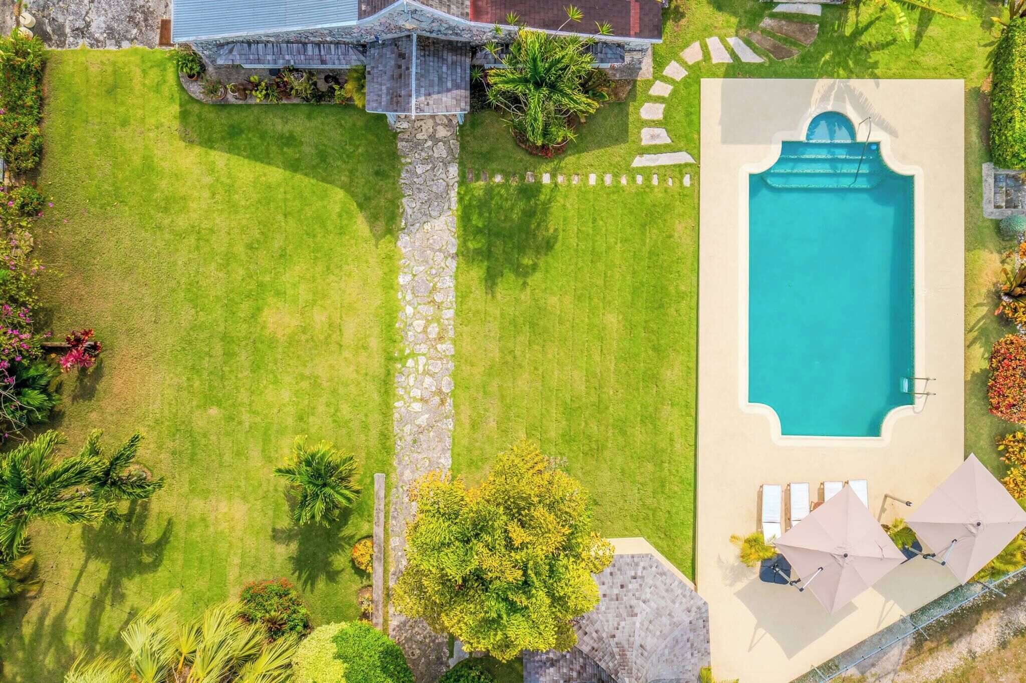 A swimming pool with a stone wall, a lawn, and a few trees.