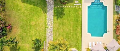 A swimming pool with a stone wall, a lawn, and a few trees.