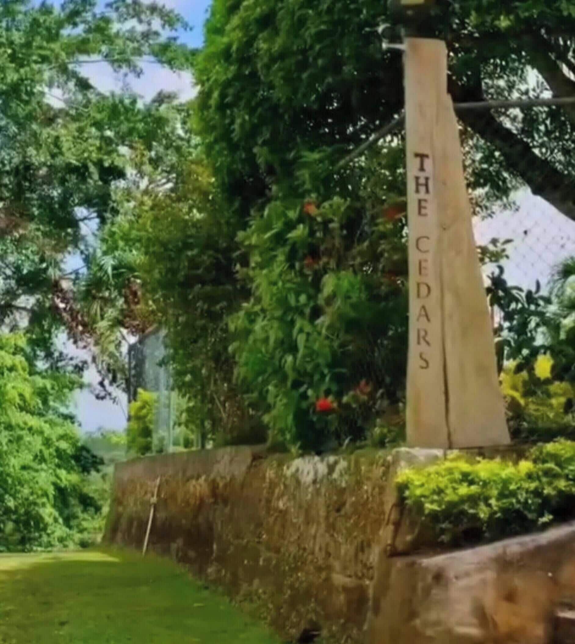 A stone monument with the inscription 'THE CEDARS' surrounded by lush greenery.
