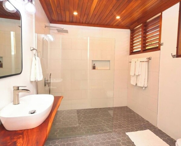 Un bany modern amb sostre de fusta, un lavabo blanc, un espai de banyera amb vidre i un sòl de rajoles hexagonals.
