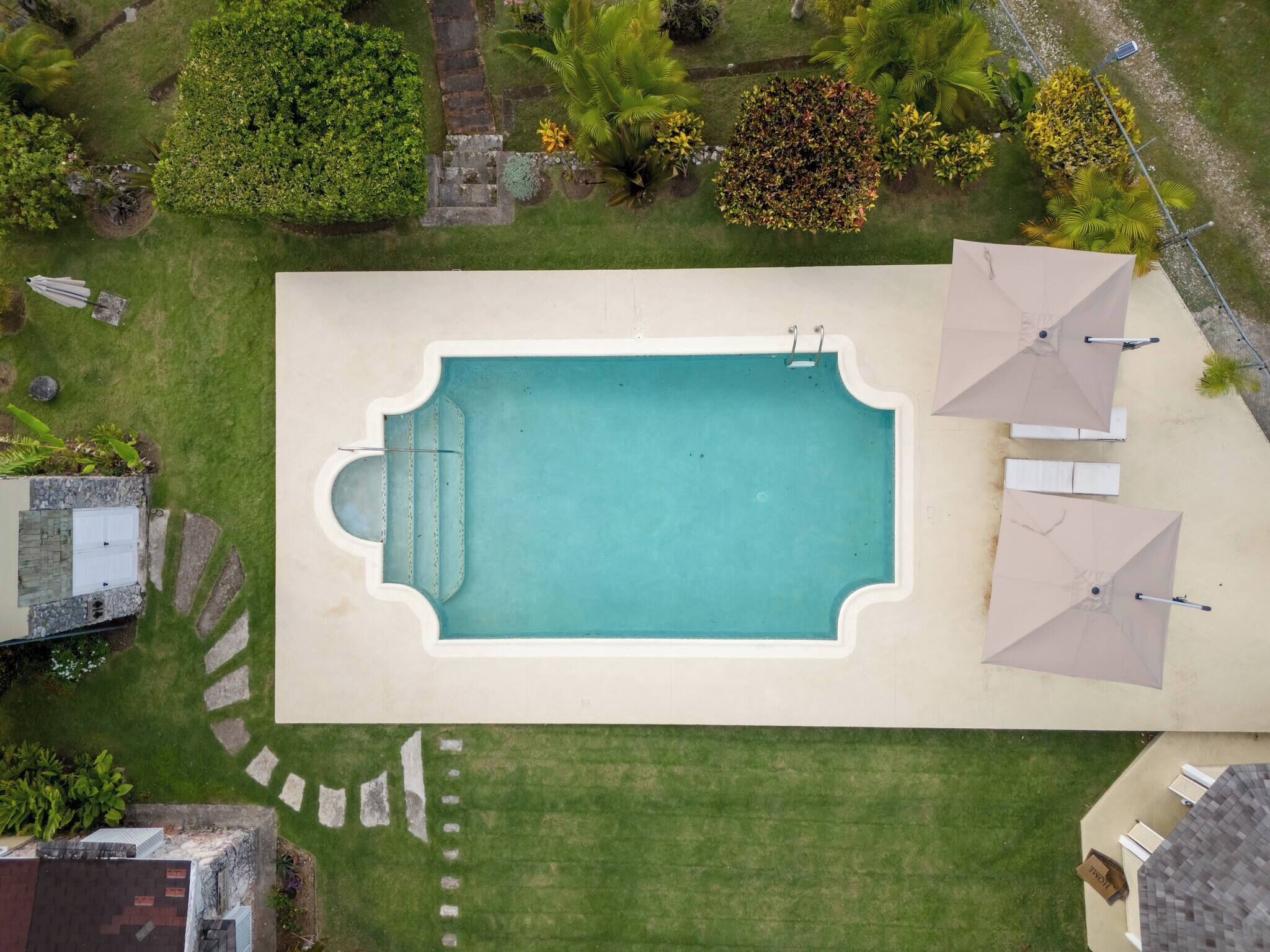 An aerial view of a rectangular swimming pool with a surrounding deck, surrounded by well-maintained lawns and various plants.