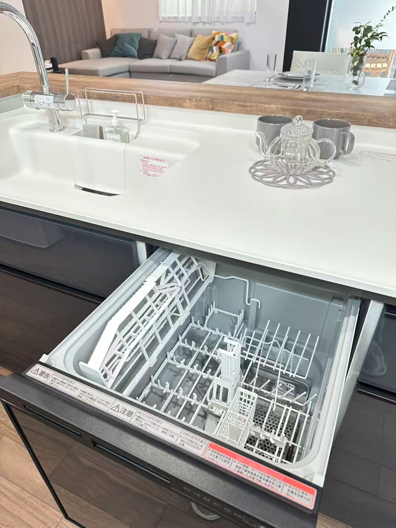 A modern kitchen with a built-in dishwasher, a stainless steel sink, and a countertop with a glass coffee pot.