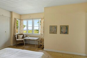 Ein Zimmer mit einem Bett, einem Tisch, zwei Stühlen, einem Fenster mit Vorhängen und zwei Bildern an der Wand.