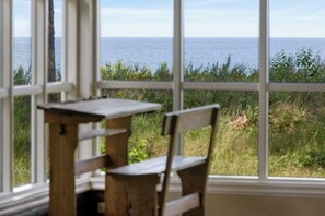Ein Zimmer mit Meerblick durch große Fenster, ein Holztisch und ein Stuhl.