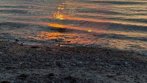 Solnedgang over et roligt hav med en klippefyldt kystlinje.