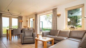 A modern living room with a sofa, chairs, a coffee table, and a dining area. - Pet-Free Texel Villa with Sauna (De Koog)