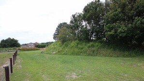 A grassy field with a wooden fence, a bench, and a building in the background. - Pet-Free Texel Villa with Sauna (De Koog)