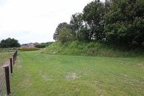 Ein grasbewachsenes Feld mit einem Holenzaun, einer Bank und einem Gebäude im Hintergrund.