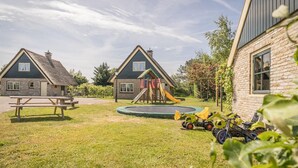 A playground with a slide and a trampoline, a picnic table, and two houses with brick exteriors. - Pet-Free Texel Villa with Sauna (De Koog)