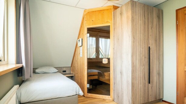 A bedroom with a bed, a wooden wardrobe, a window with curtains, and a radiator. - Pet-Free Texel Villa with Sauna (De Koog)