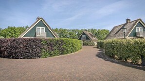 A pathway leading to traditional-style buildings with thatched roofs, surrounded by well-maintained hedges. - Pet-Free Texel Villa with Sauna (De Koog)