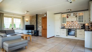 A living room with a sofa and TV, a kitchen with white cabinets, and a brick wall. - Texel Nature Villa with Sauna (De Koog)