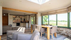 A modern kitchen with wooden beams, a dining area with chairs, and large windows with a view. - Texel Nature Villa with Sauna (De Koog)