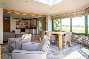 A modern kitchen with wooden beams, a dining area with chairs, and large windows with a view. - Texel Nature Villa with Sauna (De Koog)