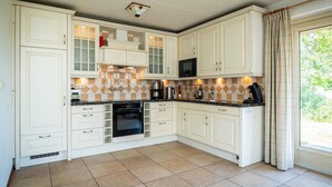 A kitchen with white cabinetry, a black oven, and a window with curtains. - Texel Nature Villa with Sauna (De Koog)