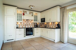 A kitchen with white cabinetry, a black oven, and a window with curtains. - Texel Nature Villa with Sauna (De Koog)