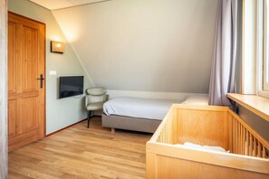 A room with a wooden door, a television, a bed, a chair, and a crib. - Texel Nature Villa with Sauna (De Koog)