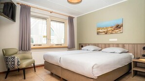 A bedroom with a bed, a chair, a window with curtains, a painting on the wall, and a light fixture. - Texel Nature Villa with Sauna (De Koog)