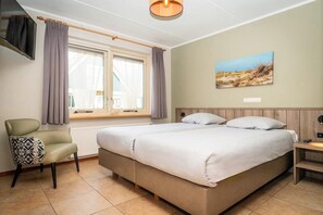 A bedroom with a bed, a chair, a window with curtains, a painting on the wall, and a light fixture. - Texel Nature Villa with Sauna (De Koog)