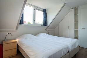 A bedroom with a bed, a nightstand, a desk lamp, a window with curtains, and built-in wardrobes. - 3-Bed Villa with Whirlpool (De Koog)