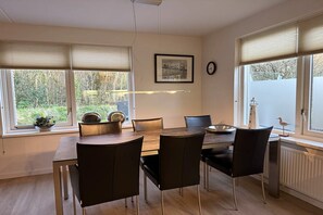 Un comedor con una mesa y sillas, una ventana con persianas, un cuadro en la pared y un reloj.