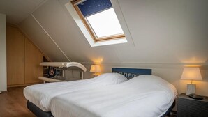 Ein Schlafzimmer mit Dachfenster, einem Bett, Nachttischlampen, einem kleinen Tisch und einem Kleiderschrank.