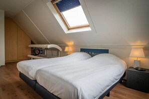 Ein Schlafzimmer mit Dachfenster, einem Bett, Nachttischlampen, einem kleinen Tisch und einem Kleiderschrank.