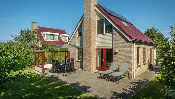 Ein Haus mit schrägem Dach, Schornstein, einer Glashaube mit Sitzgelegenheiten und einer Terrasse.